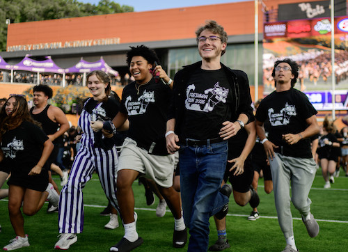 Group of eight smiling boys and girls running on stadium football field wearing matching black shirts